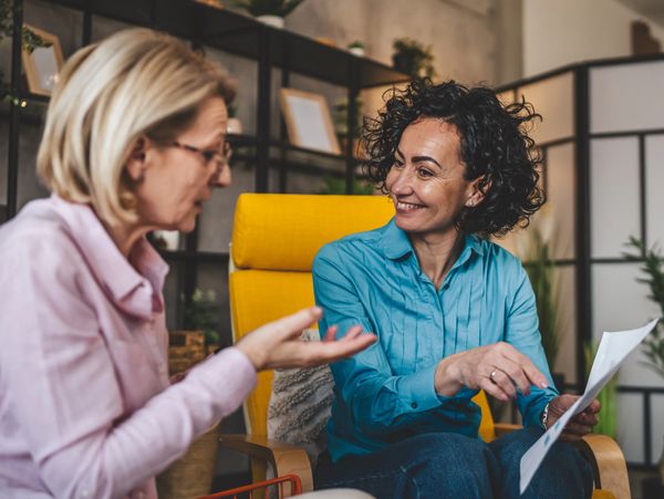 Two women engaged in a friendly discussion, one holding papers.