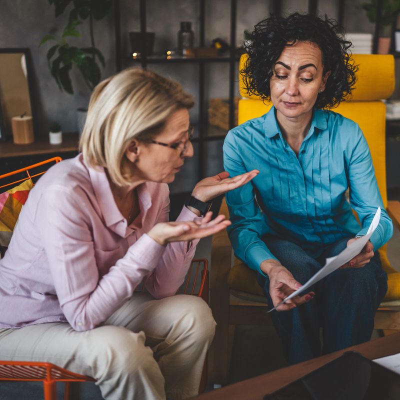 two mature women sit at home hold paper document report have consultation businesswoman talk about actual tasks and problems