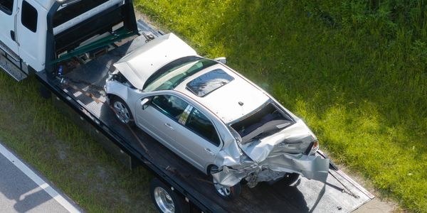 Damaged silver car with severe rear-end collision on a flatbed tow truck.