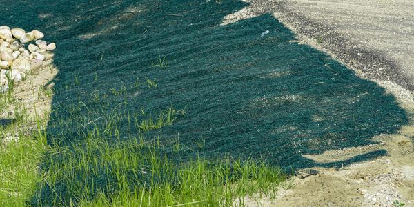 Erosion control matting on a sandy slope with grass and rocks.