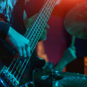 Close-up of musician playing electric bass guitar with drummer in background.