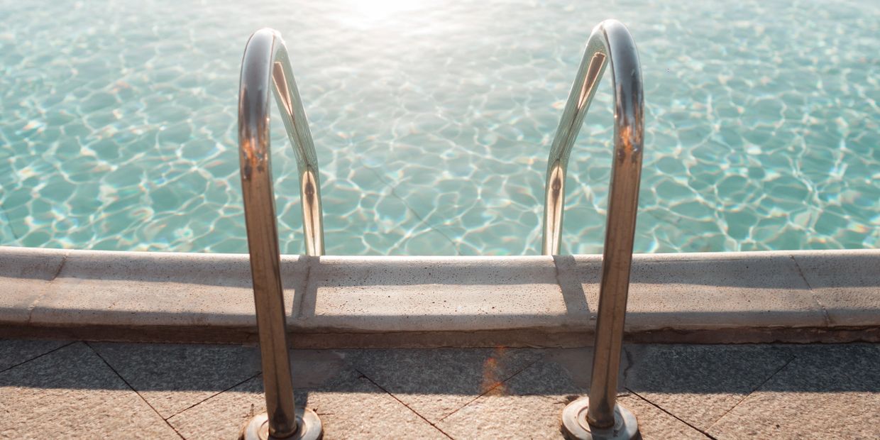 Metal pool ladder leading into a clear, sunlit swimming pool.