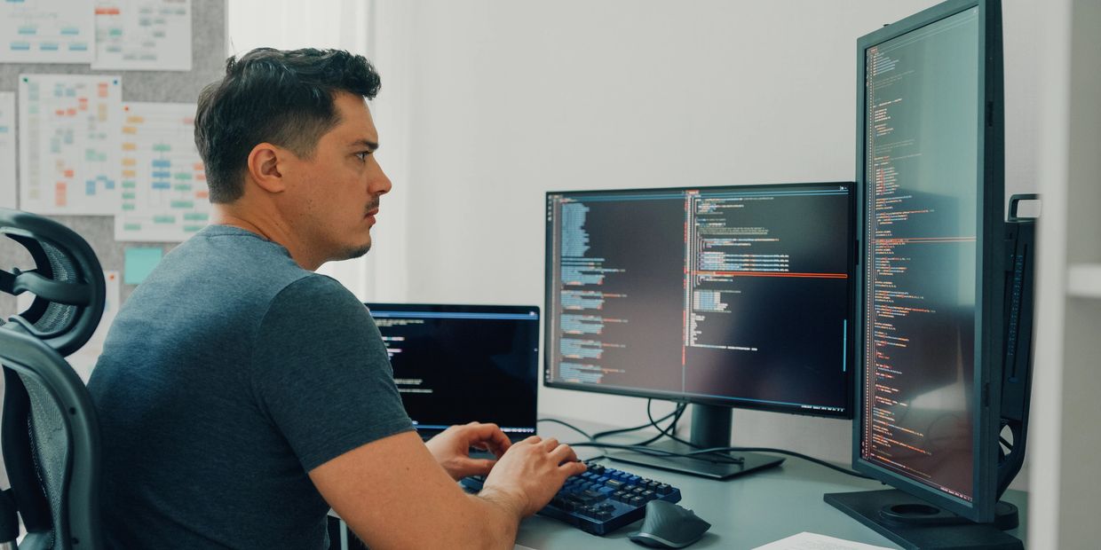 Man working on coding at a desk with multiple monitors.
