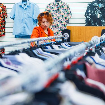 Woman browsing shirts in a clothing store with colorful shirts in the background.