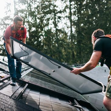 Two men installing a solar panel on a roof with trees in the background.