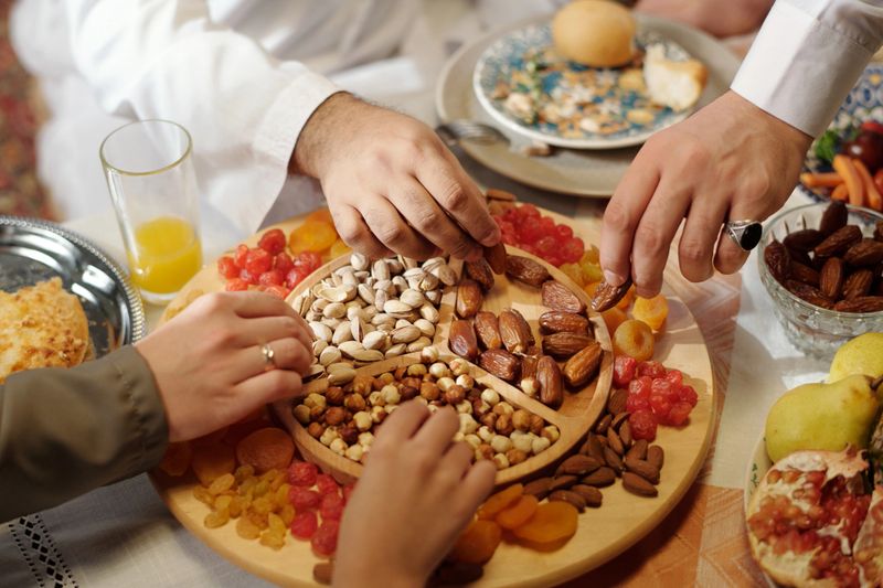 Hands of unrecognizable Muslim people taking nuts and dried fruits from platter at Islamic holiday celebration dinner