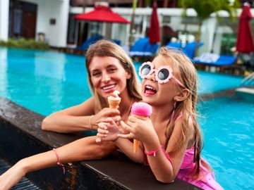 Mother and daughter enjoying ice cream by the pool on a sunny day.