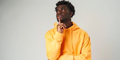 Man in orange hoodie thoughtfully looking up, finger on chin.