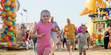 Children running happily at a vibrant carnival with families in the background.
