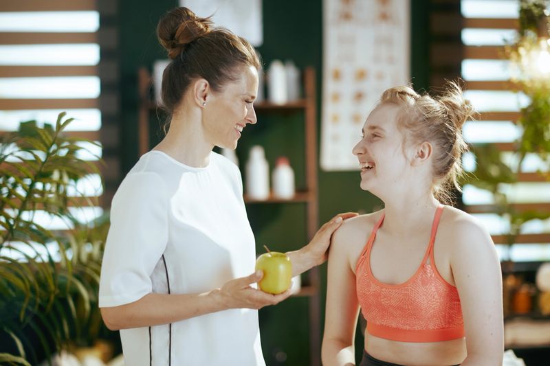 Healthcare time. smiling female medical massage therapist in massage cabinet with teenage client and an apple.