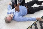 Person performing CPR on an older man lying on the floor.