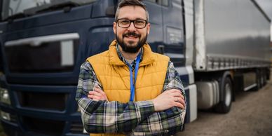 Smiling man in yellow vest stands confidently in front of a large truck.