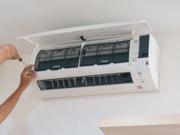 Technician repairing a wall-mounted air conditioner indoors.