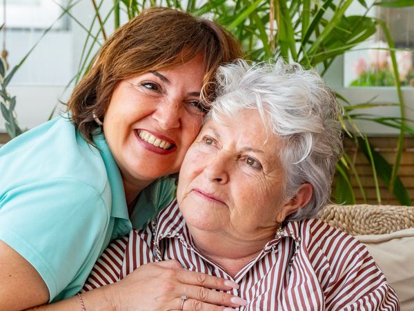 Two women sharing a tender, loving moment indoors with plants in the background.
