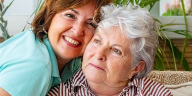 A woman warmly embraces an elderly woman indoors.