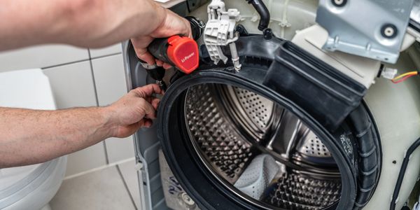 Technician repairing the front panel of a washing machine with a drill.