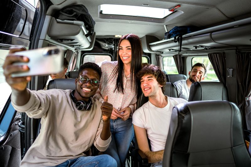 Young cheerful college friends taking selfies while traveling by bus on a field trip