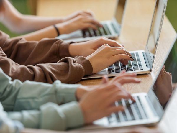 People typing on laptops in a row at a wooden table.