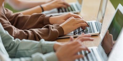 People typing on laptops in a row at a wooden table.