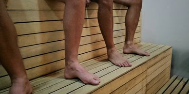 Three people sitting barefoot on wooden benches, likely in a sauna or spa.