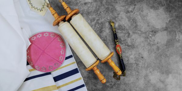 A pink kippah, a tallit, and a Torah scroll on a gray surface.
