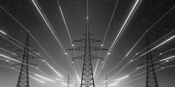 High-voltage power lines glowing with blue and orange light against a starry night sky.
