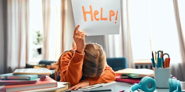 Child overwhelmed with homework holding a 'HELP!' sign.