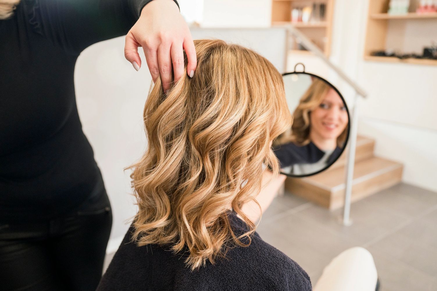 Woman with freshly styled blonde curly hair admiring in mirror.