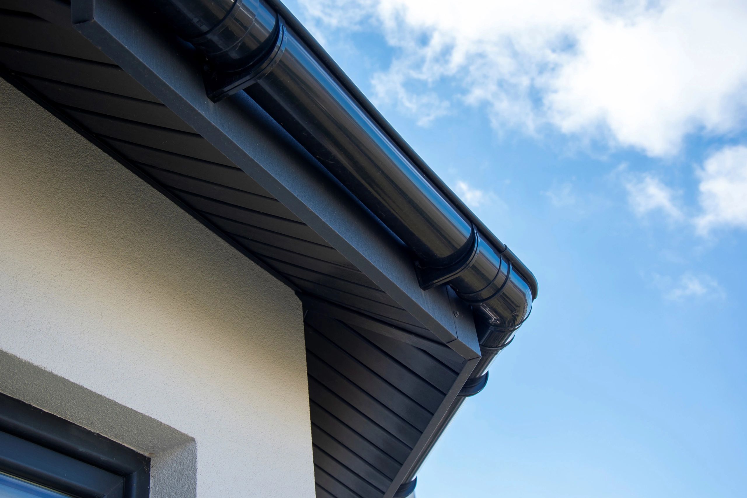 Close-up of a black rain gutter on a house roof against a blue sky.