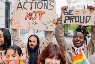 People hold signs promoting pride and action in a lively crowd.
