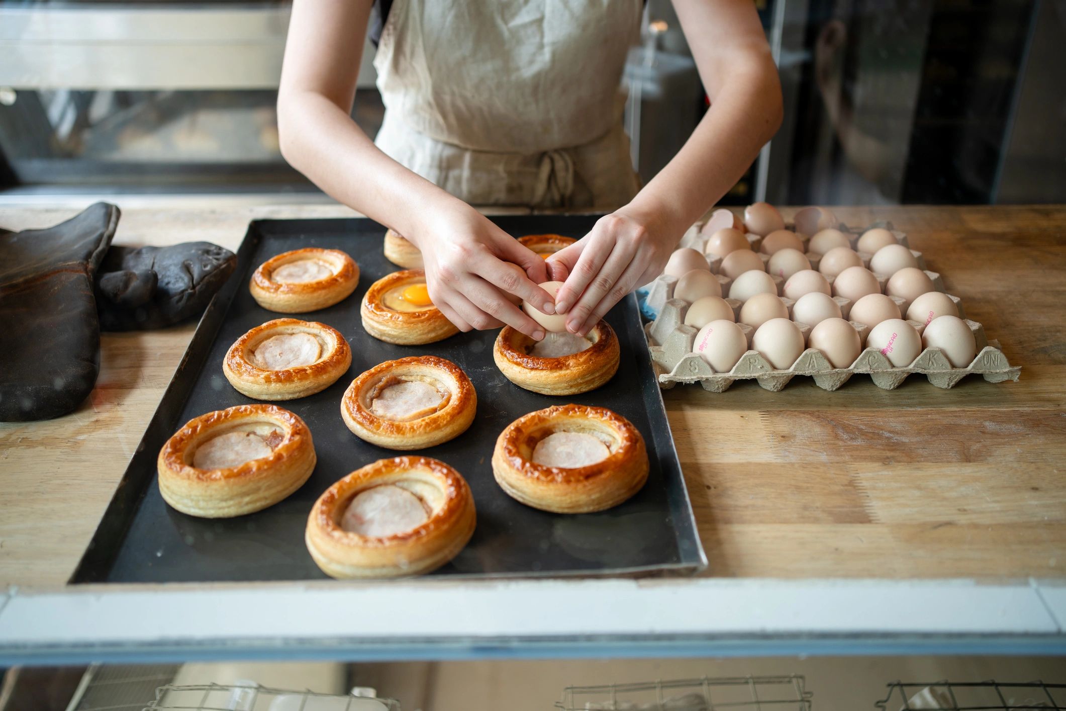 A baker preparing nut-topped pastries on a baking tray.
