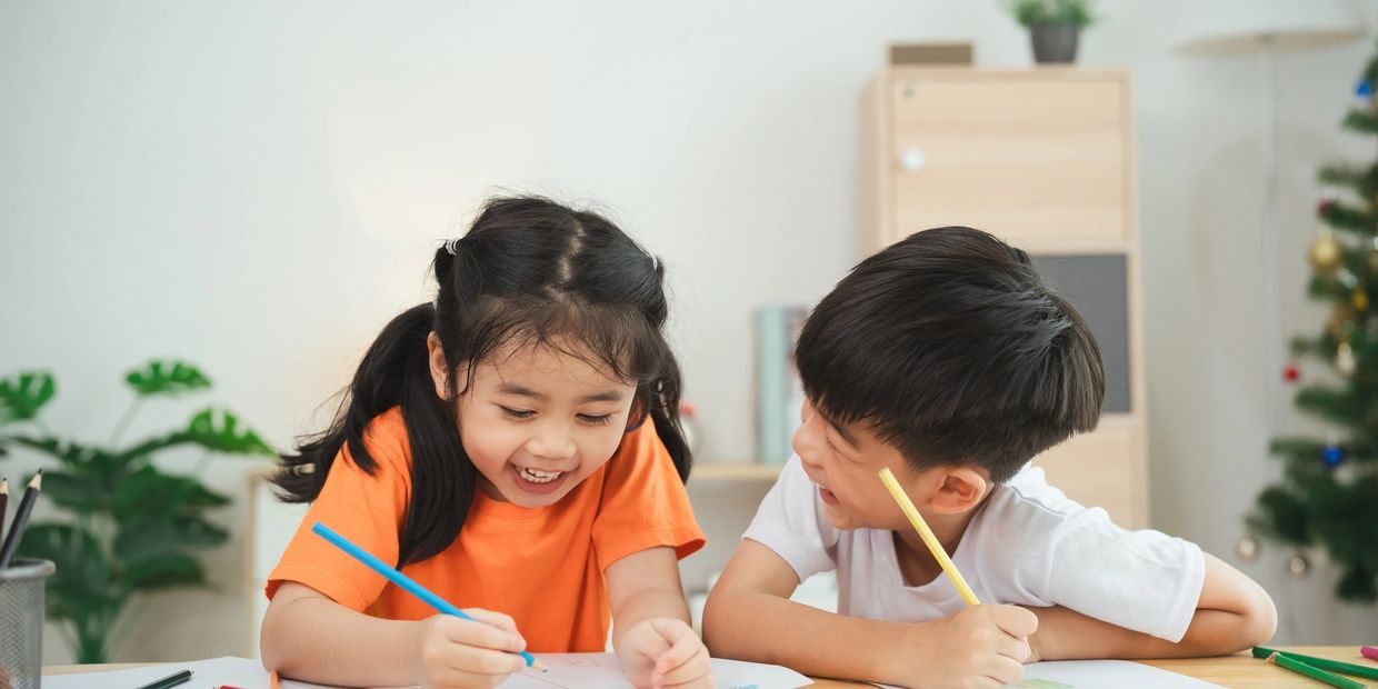 Two children happily drawing and coloring together at a table.