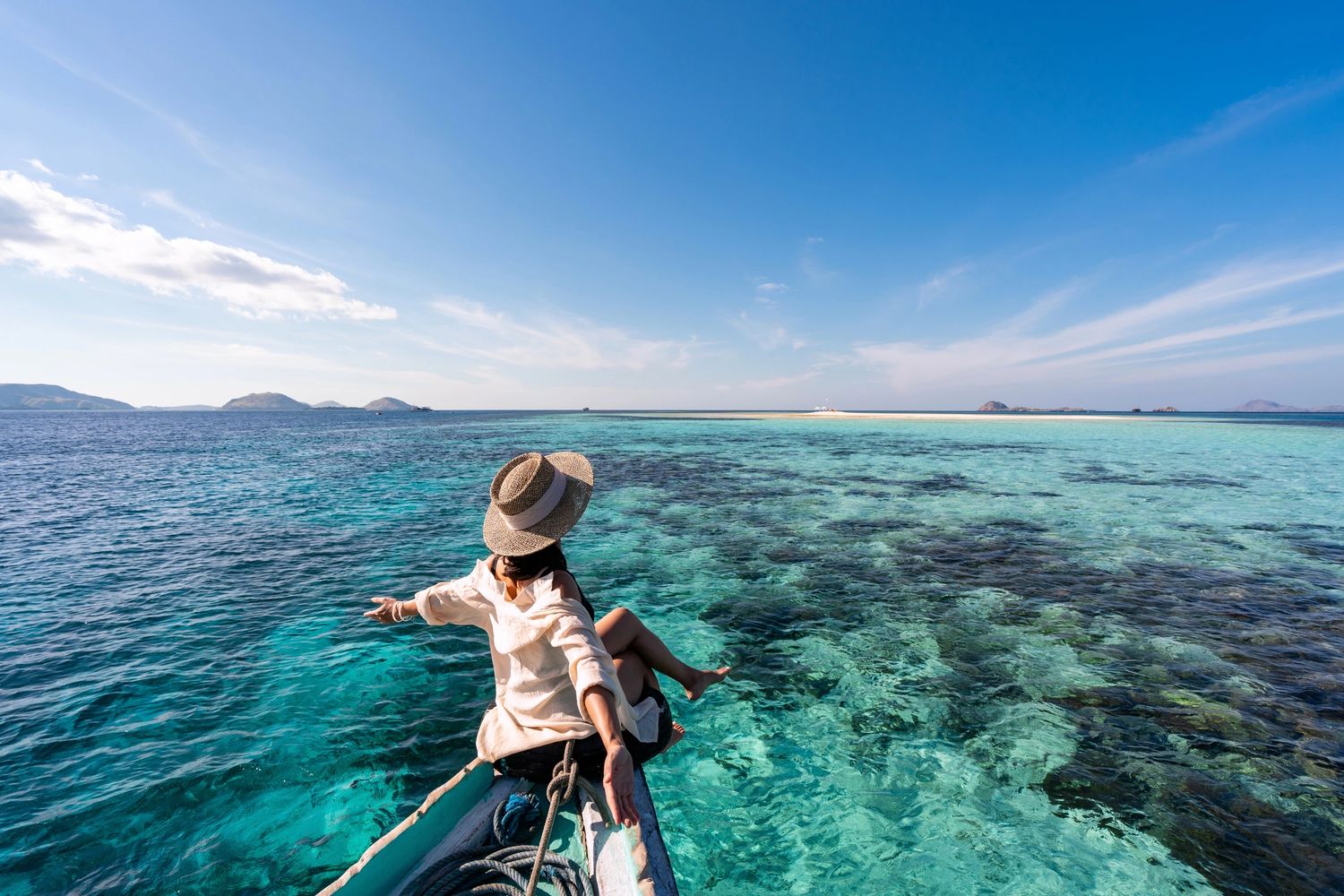 Woman enjoying serene ocean view from a boat's bow under clear blue skies.