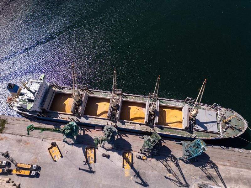 Aerial view of big cargo ship bulk carrier is loaded with grain of wheat in port at sunny day.