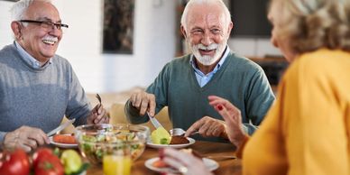 Three older adults enjoying a meal and conversation around a table.