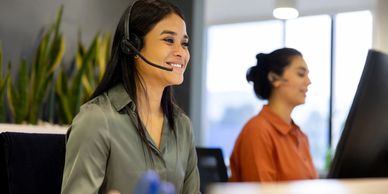 Two women working in a call center, wearing headsets and smiling.