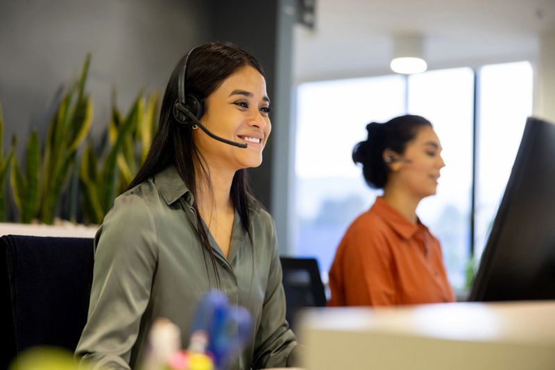 Happy Latin American businesswoman using a headset while making a video call at the office and smiling
