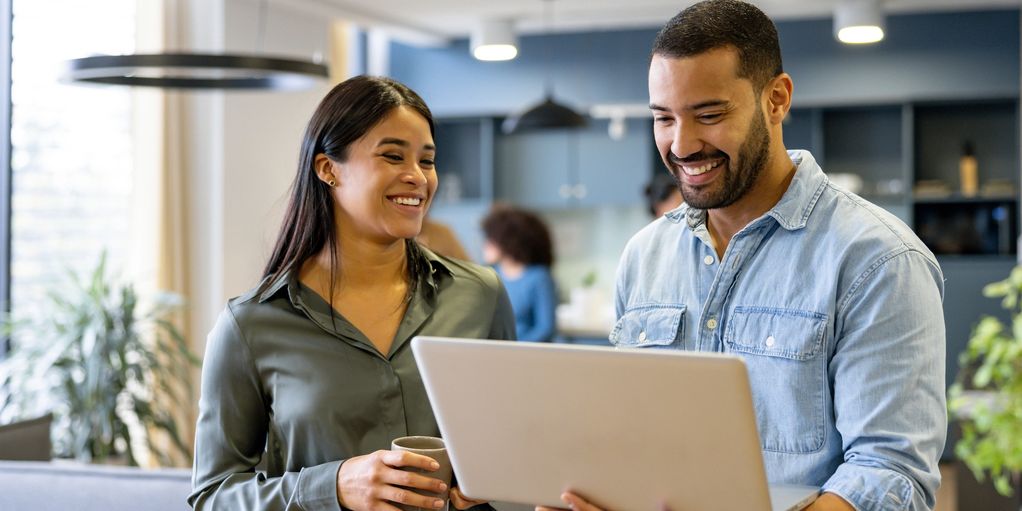 Two coworkers sharing a smile while looking at a laptop in a modern office.
