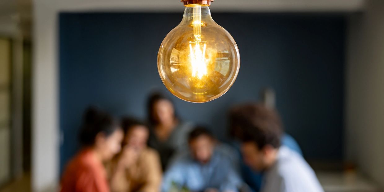 Glowing light bulb with a group of people brainstorming in the background.