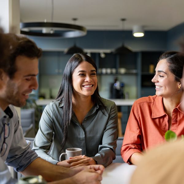 Three colleagues happily chatting during a coffee break in a modern office.