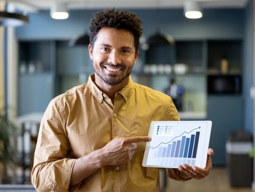 Man smiling and pointing at a rising bar graph on a tablet.
