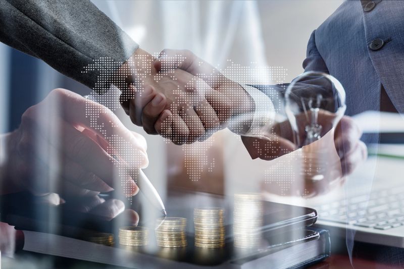 Double exposure of a handshake and a working manager on a computer.