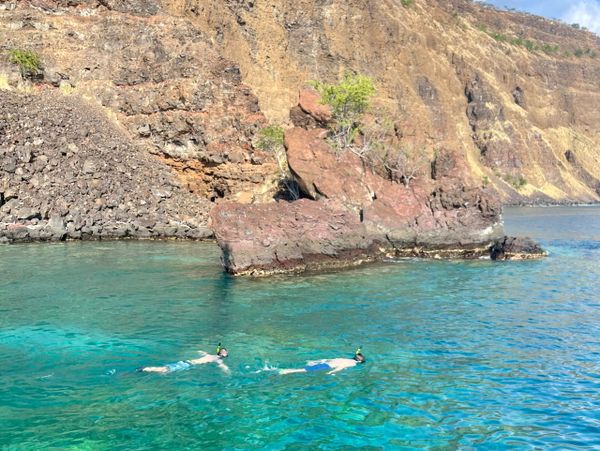Two snorkelers explore clear blue waters near rocky cliffs under a sunny sky.