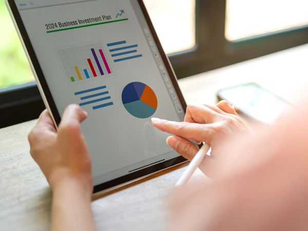 Person reviewing a 2024 business investment plan on a tablet with charts.
