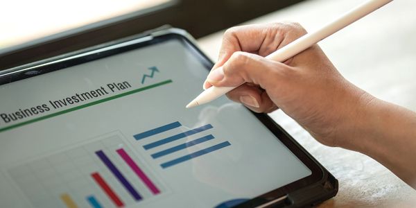 A person uses a stylus on a tablet displaying a business investment plan with charts.