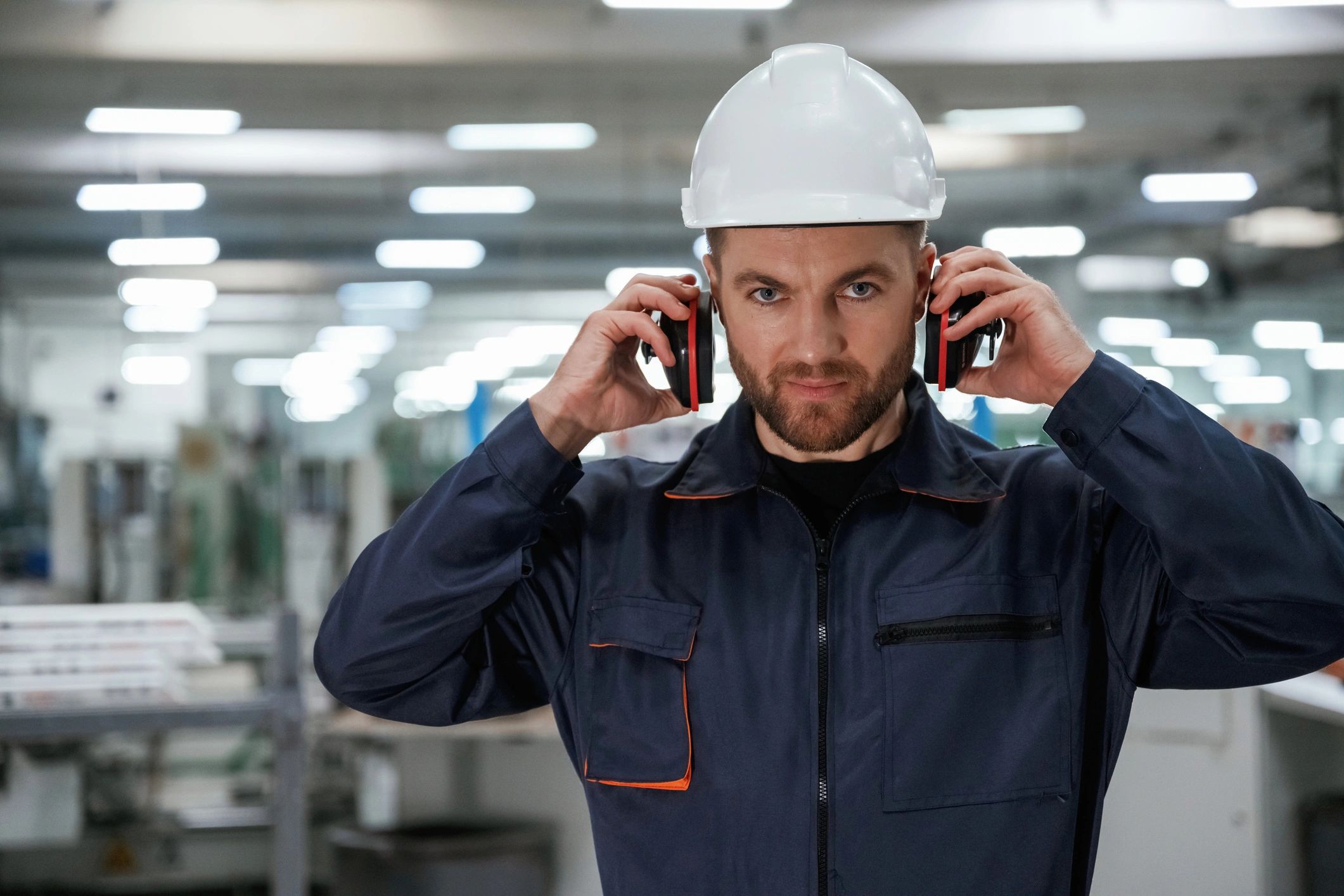 Worker in a hard hat putting on earmuffs in a factory