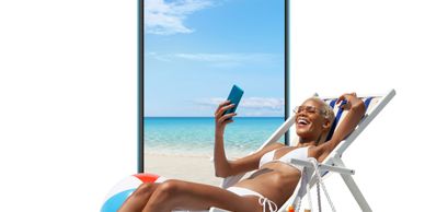 Woman in bikini relaxing on a beach chair taking a selfie.