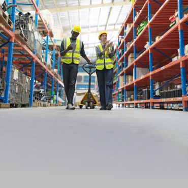 Two warehouse workers in safety gear discussing inventory.