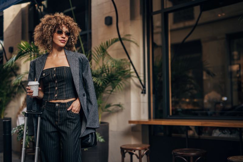 Stylish woman with curly hair sips coffee on a vibrant city street