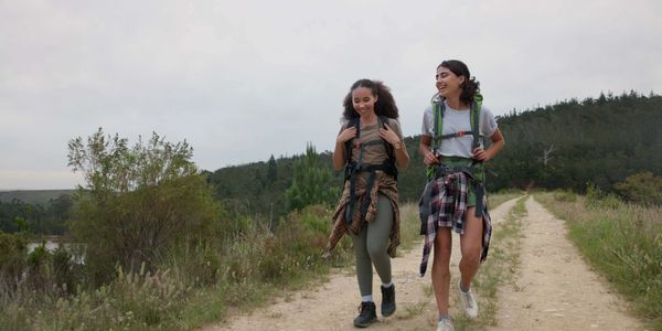 Two women hiking and smiling on a trail in nature.